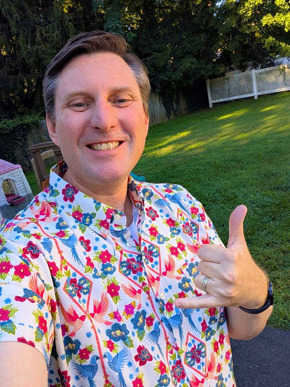 John Daly smiling outdoors in a colorful floral shirt and giving a shaka gesture